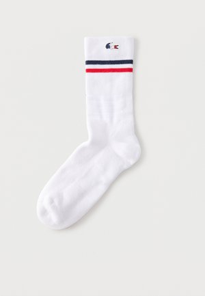 Fehér sportzokni sötétkék és piros csíkokkal a tetején, és a csíkok felett egy kis hímzett krokodil logóval.