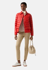 Red puffer jacket with a cropped design, striped long-sleeve shirt, beige trousers, and white sneakers. Handbag is a soft beige.