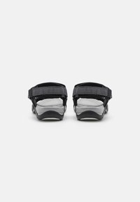 Sandales noires avec des brides en tissu texturé, ajustables au talon et à l'avant du pied. Semelle en caoutchouc avec une semelle intérieure rembourrée et ergonomique.