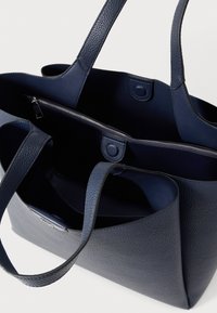 Τσάντα tote από δέρμα σε ναυτικό μπλε με υφή, διαθέτει δύο χειρολαβές και εσωτερικό διαμέρισμα με φερμουάρ. Κομψός, απλός σχεδιασμός.