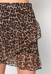 Leopardmønstret nederdel med flæser, der har et gennemsigtigt overlay. Farvepaletten inkluderer nuancer af brun, sort og tan. Tekstureret fabriksdetalje.