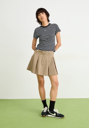 Pruhované čierno-biele tričko, béžová plisovaná sukňa, čierne tenisky s bielymi akcentmi, kombinované s čiernymi ponožkami po členky.