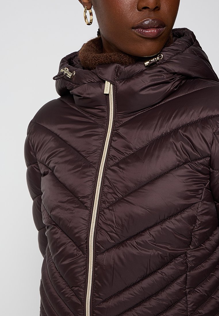 Brązowa kurtka puchowa z wzorem w romby, z zamkiem z przodu oraz kapturem z miękkim brązowym wykończeniem. Srebrne akcenty.