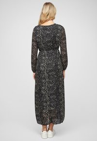Long black dress with a flowing silhouette, featuring a textured gold wave pattern, long sleeves, and a cinched waist. Worn with white sneakers.