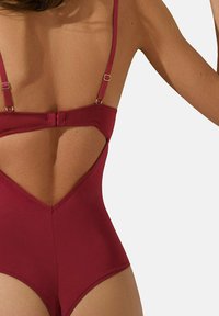 Maillot de bain bordeaux avec un décolleté en V profond dans le dos, des bretelles ajustables et des accents en métal doré. Texture lisse et design ajusté.