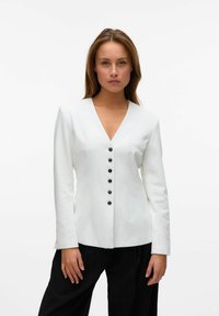 Blazer blanco ajustado con escote en V, mangas largas y seis botones negros en la parte delantera. Textura suave y diseño estructurado.