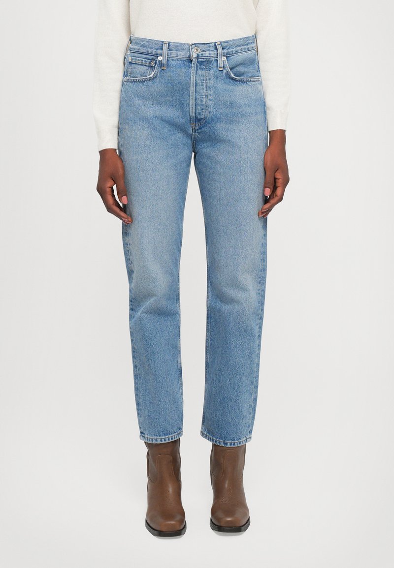 Light blue denim jeans with a high waist, straight fit, five pockets, and silver hardware details. Paired with brown ankle boots.