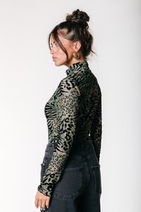 Haut à manches longues et col haut en tissu transparent, avec un mélange de motifs animaliers en vert, noir et beige ; associé à un jean noir taille haute.