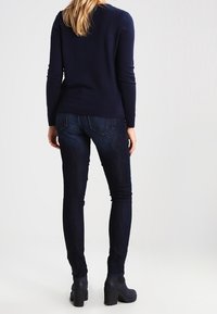 Suéter navy, diseño ajustado, mangas largas, combinado con jeans oscuros ajustados. El conjunto incluye botas negras de tobillo gruesas.