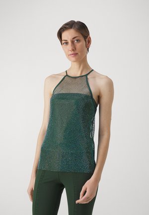 Haut halter en maille verte avec un design ajusté, mettant en valeur un tissu texturé et un tissage ouvert. Associé à un pantalon ajusté vert assorti.