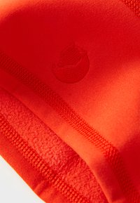 Close-up of bright orange fabric with detailed stitching and an embroidered logo of a curled fox.