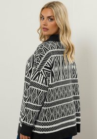Schwarzer und weißer gemusterter Pullover mit geometrischen Designs, einem hohen Ausschnitt und einer lockeren Passform mit gerippten Bündchen und Saum.