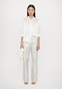 Witte zijden blouse met lange mouwen, gecombineerd met glanzende zilveren wijde broek. Accessoires zijn een lichtgekleurde sjaal.