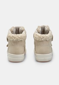Beżowe buty za kostkę z miękkim, futrzanym kołnierzem, paskiem na rzep, teksturowanym zamszowym materiałem oraz białą gumową podeszwą z różowymi akcentami.