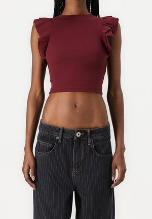 Bordeauxrode, geribbelde cropped top met gerimpelde schouderdetails, gecombineerd met zwarte, hooggetailleerde broek met krijtstrepen. Soepele textuur, nauwsluitend ontwerp.