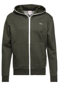 Mörkgrön zip-up hoodie med vit dragkedja, framfickor, huva och liten Lacoste krokodil-logotyp på bröstet.