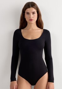 Svart långärmad bodysuit tillverkad av mjukt, stretchigt tyg; har en scoop-halsringning och en figurnära silhuett, med hög skärning vid benen.
