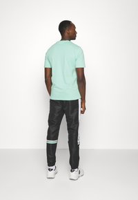 Mintgroene t-shirt met korte mouwen, gecombineerd met zwarte trainingsbroeken met witte accenten en een teal strook bij de manchetten.