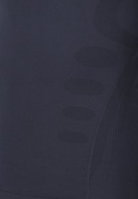 Granatowa tkanina sportowa z teksturowanymi wzorami, gładkimi sekcjami i akcentami tekstylnymi, o okrągłym kształcie i oddychających obszarach siateczkowych.