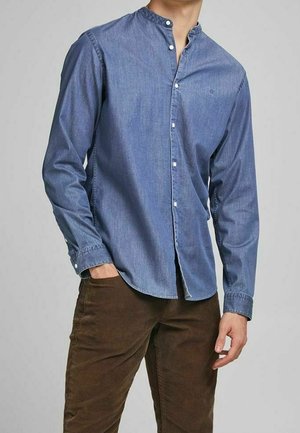 Chemise en denim bleu à boutonnières avec col montant, manches longues et coupe ajustée. Associée à un pantalon en velours côtelé marron. Texture lisse.
