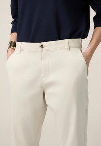 Pantalons en mélange de coton beige avec une coupe droite, poches avant et fermeture à bouton embossé unique. Texture lisse et couture minimale.