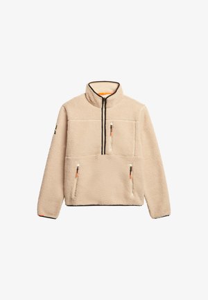 Beżowy polarowy pulower z wysokim kołnierzem, półzamkiem z przodu, dwoma kieszeniami na zamki na piersi i elastycznymi mankietami. Teksturowany, ciepły materiał.