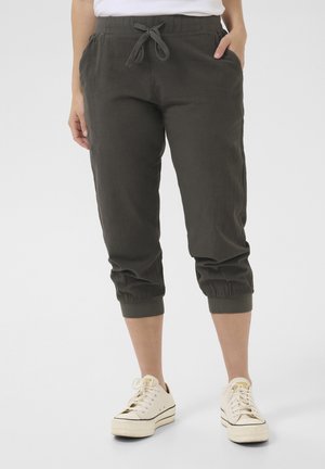 Dunkelgrüne, leichte Jogginghosen mit elastischen Bündchen und Bund, ausgestattet mit Seitentaschen und Kordelzug. Kombiniert mit weißen Turnschuhen.
