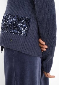 Maglione in maglia blu navy con design a costine testurizzate e tasca sul retro decorata con paillettes. Materiale morbido e vestibilità comoda.