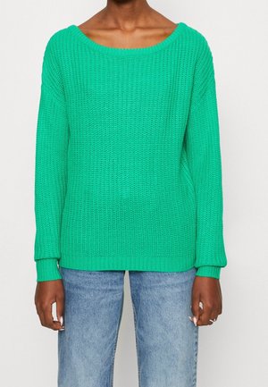 Groene gebreide trui met een brede bootnek, geribbelde manchetten en zoom, en een losse pasvorm, gecombineerd met lichtblauwe denim jeans.