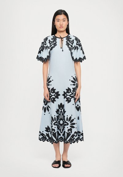 Helles blaues Kleid mit schwarzen Blumenmustern, kurzen schwingenden Ärmeln, rundem Ausschnitt und gewelltem Saum. Getragen mit schwarzen Sandalen.