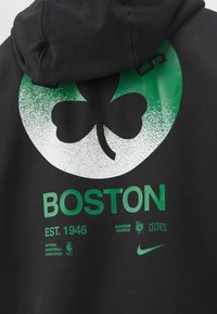 Sweat à capuche noir avec un grand graphisme vert et blanc représentant un trèfle et le mot "BOSTON" en lettres majuscules vertes. Comprend "EST. 1946" et des logos.