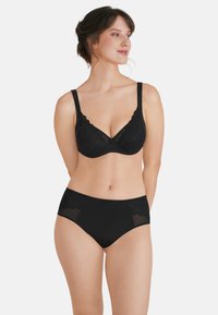 Set di biancheria intima composto da reggiseno in pizzo nero e mutandine a vita alta, caratterizzato da motivi floreali, dettagli trasparenti e bordi ondulati per un tocco di eleganza.