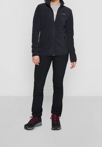 Merinovillainen tikkitakki, jossa on korkea kaulus, vetoketjukiinnitys ja kaksi sivutaskua. Yhdistetty mustiin housuihin ja vaelluskengiin, joissa on vaaleanpunaiset nauhat.