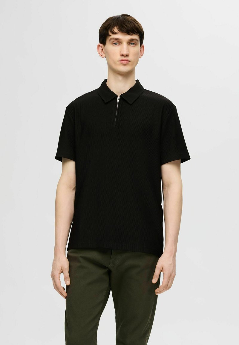 Czarna koszulka polo z krótkim rękawem i zamkiem przy kołnierzyku, wykonana z tekstury prążkowanej, zestawiona z oliwkowymi spodniami. Czysty, minimalistyczny design.