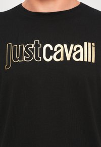 Melnas kokvilnas t-krekls ar zelta metalizētu tekstu "Just Cavalli". Klasiska apaļā kakla dizains un mīksta tekstūra ar brīvu piegriezumu.