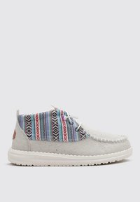 Zapato textil gris con parte superior de tela a rayas multicolor, suela de goma blanca y costura en contraste. Presenta dos ojales para los cordones.