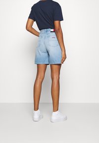 Jeansshorts i ljusblå tvätt; hög midja, femficksdesign, märkesresår. Kombineras med en marinblå t-shirt och vita sneakers.