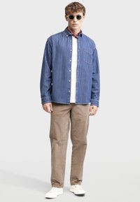 Blue and white striped button-up shirt, beige pants, and white sneakers. Includes a chest pocket and round sunglasses. Simple, casual style.