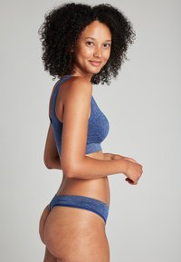 Niebieski stanik sportowy o miękkim materiale i plecze w stylu wyścigowym, w połączeniu z dopasowanymi, niebieskimi majtkami w stylu bikini, ukazującymi gładką strukturę i dopasowanie.