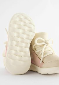 Scarpe high-top beige con accenti rosa, suola in gomma testurizzata e lacci crema. La parte superiore è in pelle liscia con dettagli cuciti.