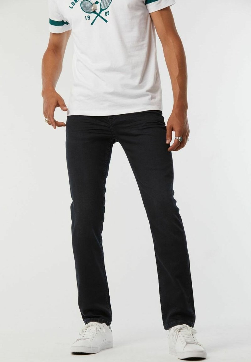 Jeans slim noirs avec une texture douce, associés à un T-shirt blanc avec des accents verts et un graphique de tennis. Baskets blanches.