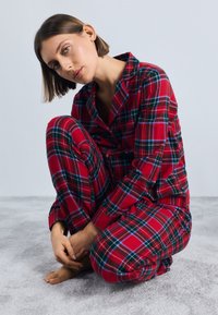 Rød og grønn rutete pysjamassett i myk stoff, med en knappetopp og elastisk livbukse, med oppbrettede ermer og en avslappet passform.