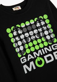 Sort bomulds T-shirt med et grafisk design af skiftende grønne og grå cirkler. Teksten "GAMING MODE" er fremtrædende i hvid.