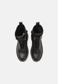 Botas de tobillo de cuero negro con punta redonda, diseño de cordones, cremallera lateral y suela texturizada. El interior presenta un forro suave.