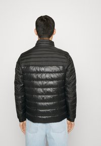 Giacca a vento nera con design trapuntato, colletto alto e polsini elastici. Finitura liscia e lucida, leggera e isolante.