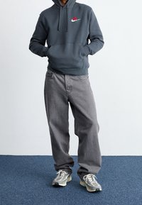 Mörkgrå hoodie med en ros-grafik, i kombination med lösa grå jeans och ljusgrå sportskor med detaljer.