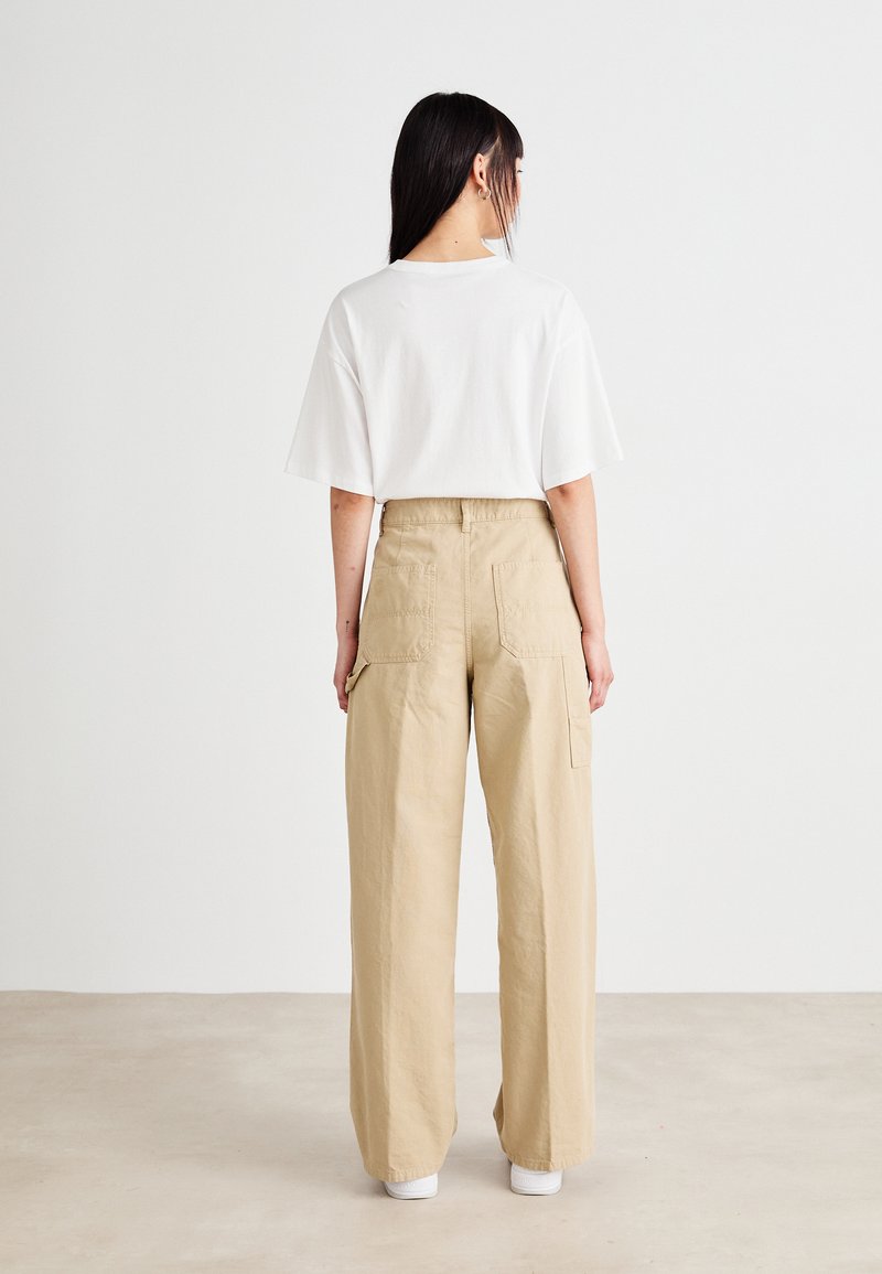 Maglietta bianca a maniche corte abbinata a pantaloni cargo larghi color beige con due tasche posteriori, realizzati in tessuto leggero.