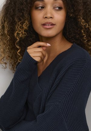 Mörk marinblå V-ringad tröja med ribbat mönster, förlängda ärmar och en avslappnad passform. Slät tyg framhäver en avslappnad design.