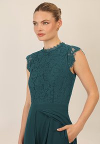 Teal kanten jurk met korte mouwen, gegolfde halslijn en een vloeiende rok. Heeft ingewikkelde bloemenpatronen en een soepele textuur.