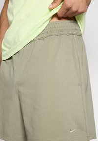 Σορτς Nike σε ανοιχτό χακί, με ελαστική μέση, πλαϊνή τσέπη και εμφανείς ραφές. Το υλικό φαίνεται μαλακό και ελαφρύ.